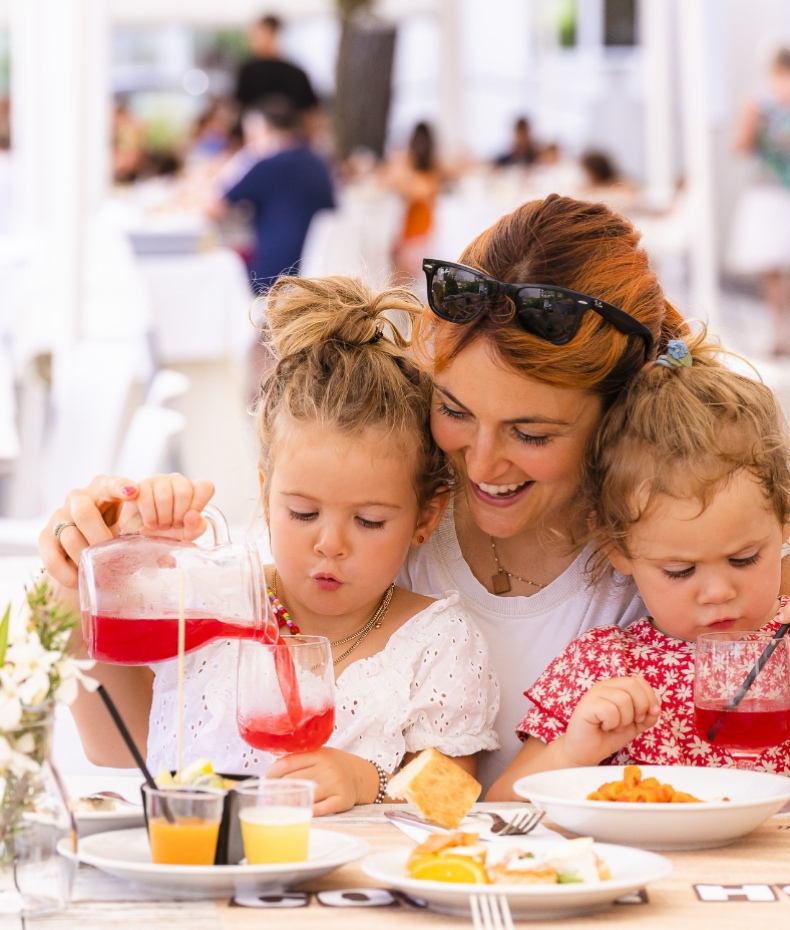 Madre e figlie sorridono mentre versano succo a tavola in un ristorante.