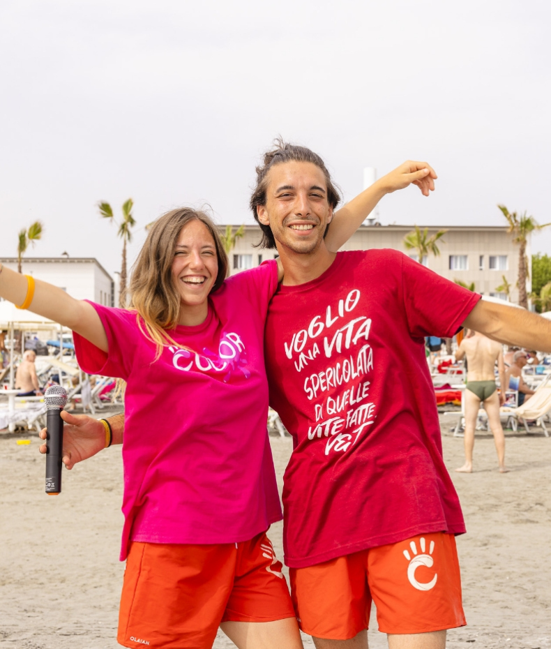 Two smiling young people on the beach, wearing colorful shirts, radiating joy.