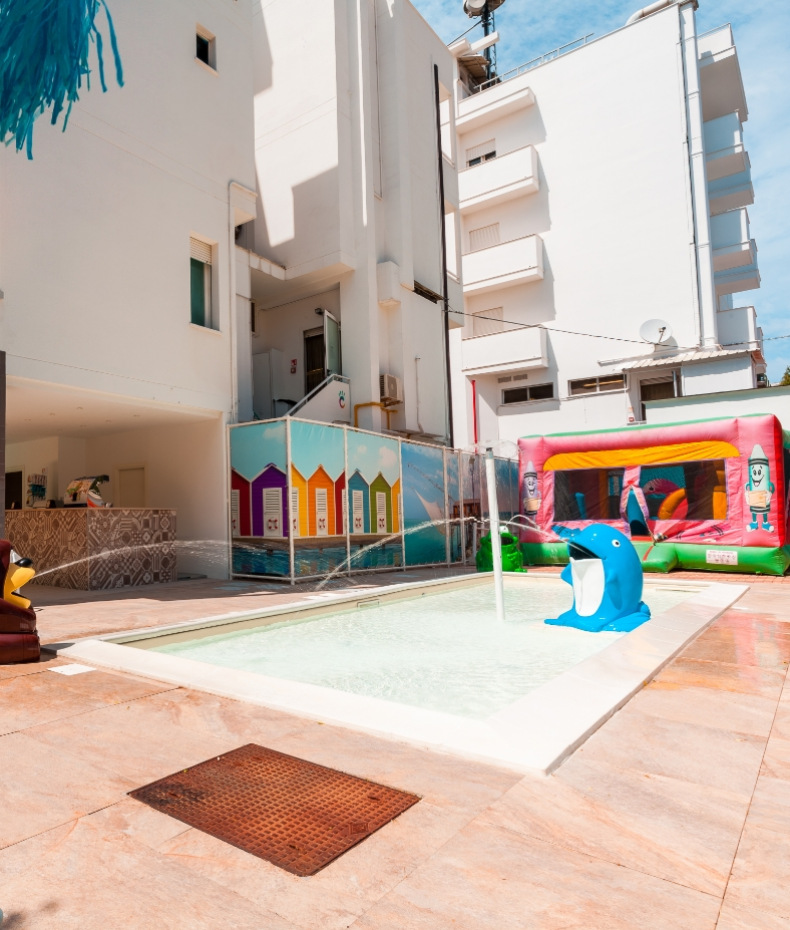 Piscina per bambini con giochi d'acqua e gonfiabile colorato in cortile soleggiato.