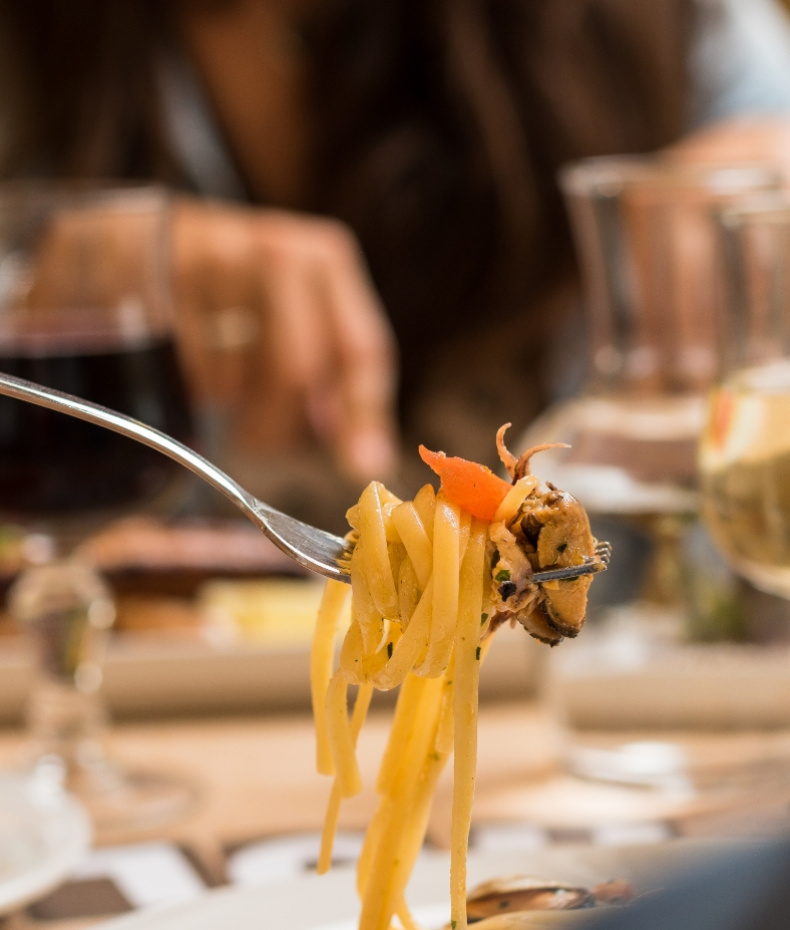 Forchetta con spaghetti, frutti di mare e vino in sfondo sfocato.